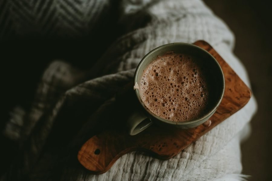 Tasse de chocolat chaud posée sur une planche en bois, au creux d'un plaid